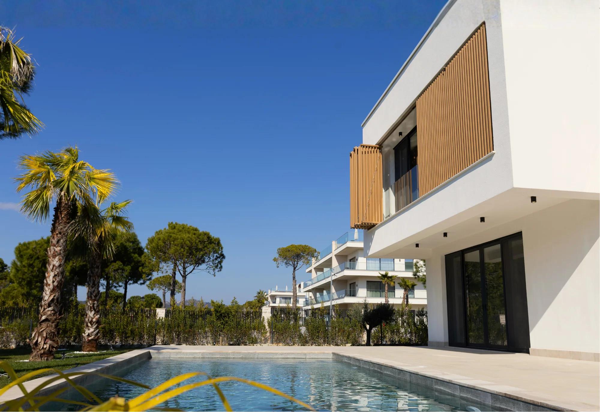 A villa's timber-shuttered facade beside the pool at dusk